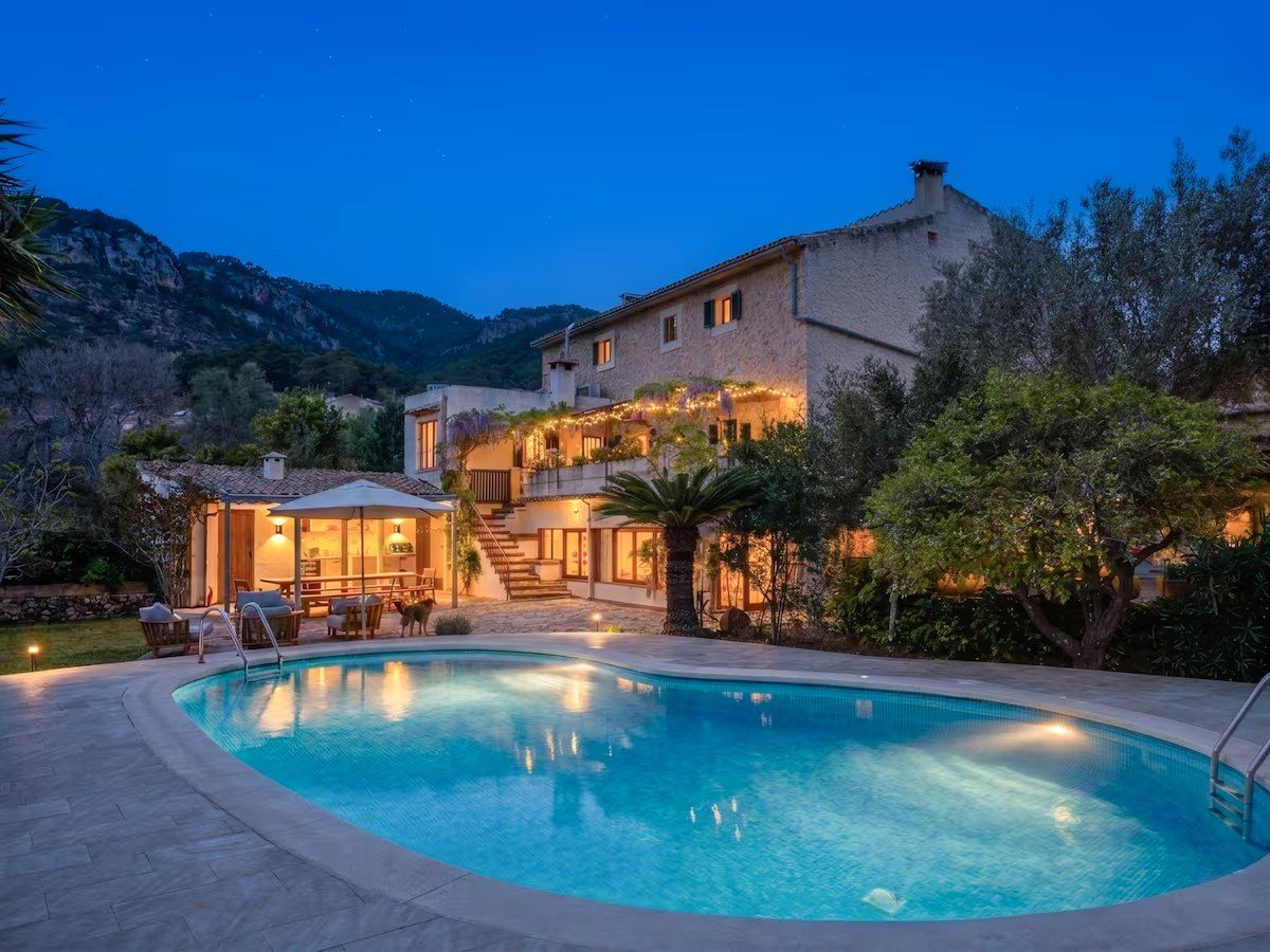 Stone villa lit up at dusk above its pool, with mountains behind